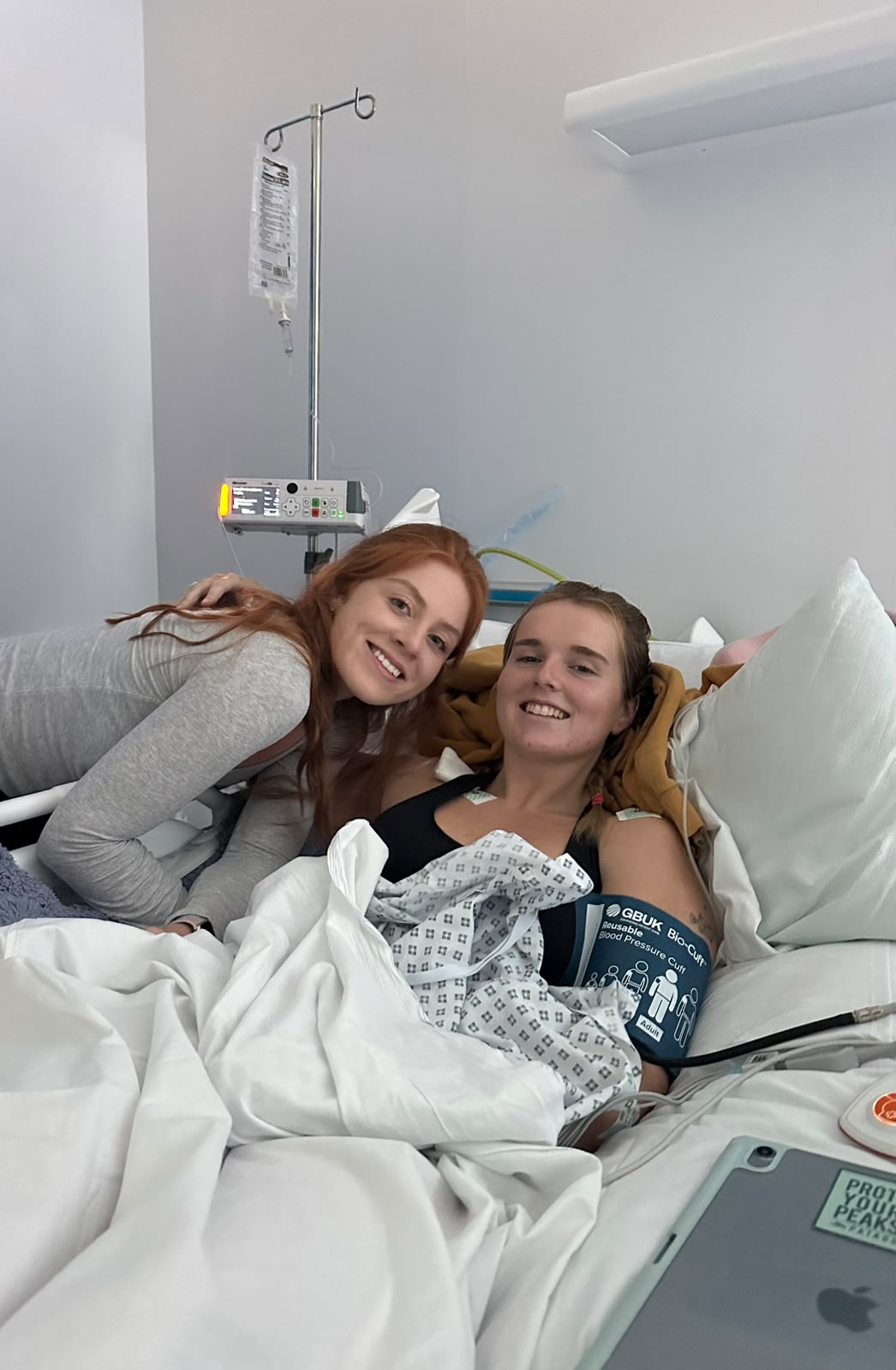 Georgia in a hospital bed with a visitor leaning in beside her, both smiling