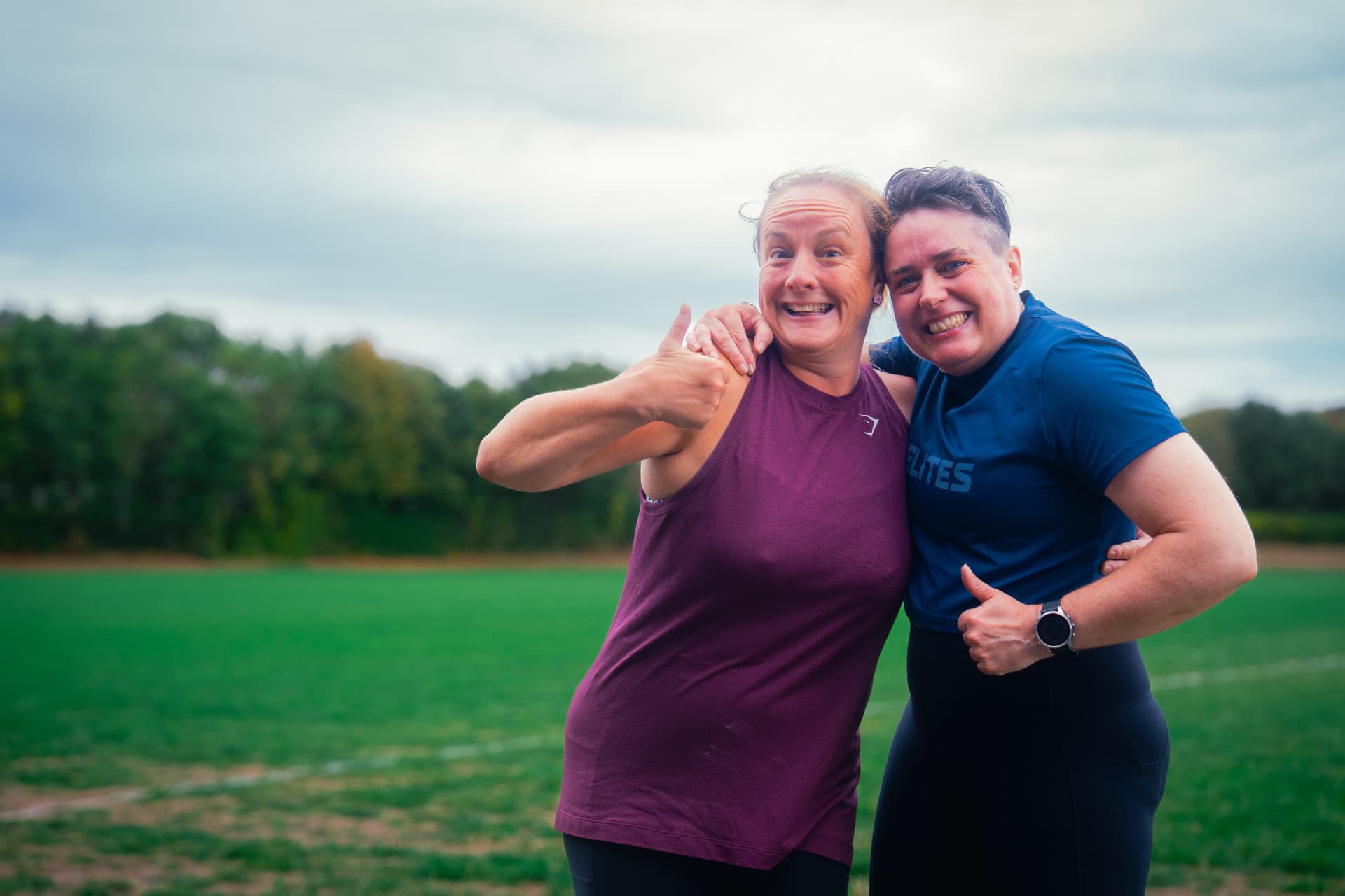 Two members hugging and giving a thumbs up on the field
