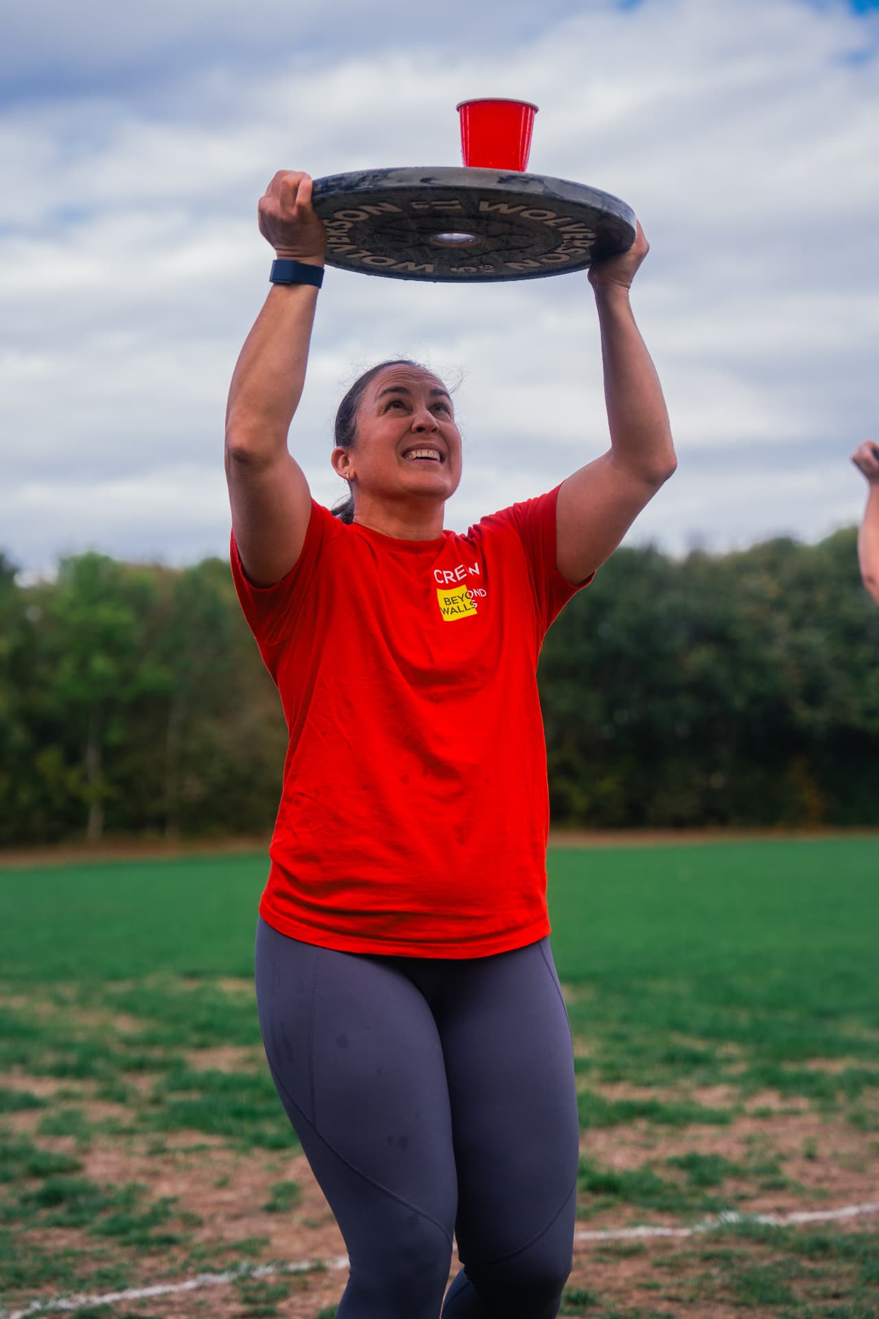 A Beyond Walls coach holding a weight plate overhead during the relay