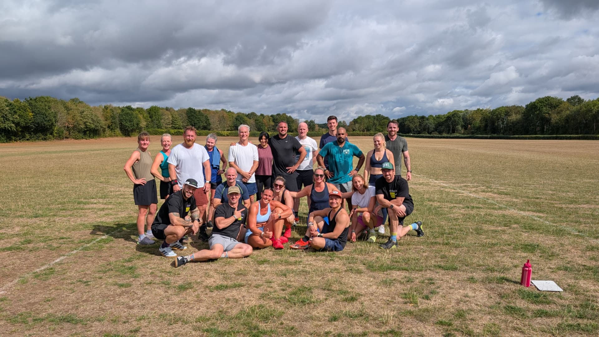 A large group of Beyond Walls members and coaches smiling together on a grass field after an outdoor session
